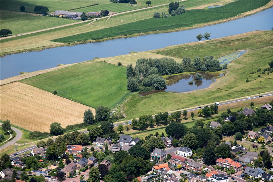Een luchtfoto van een stuk dijk waarop een dorp en de IJssel zichtbaar zijn.
